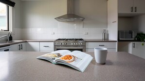 A modern kitchen with white cabinets, a stainless steel range hood, and a countertop with a magazine and a white mug.