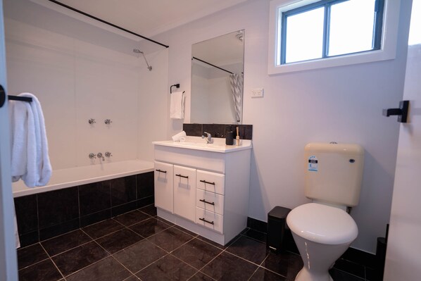 A modern bathroom with a bathtub, a toilet, a sink, and a large mirror. - Spacious Kerang Retreat | Stylish & Cosy (Kerang)