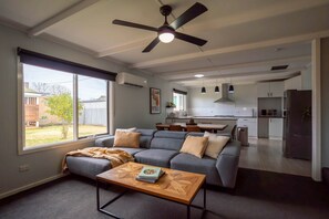 A modern living room with a grey sofa, a wooden coffee table, and a ceiling fan. - Spacious Kerang Retreat | Stylish & Cosy (Kerang)