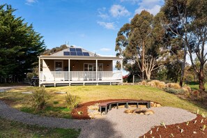 Una casa de dos plantas con balcón, paneles solares en el techo y un jardín ajardinado con una fogata.