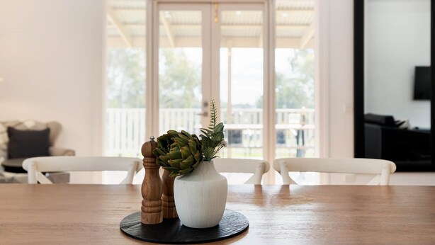 A dining table with a white vase containing green plants and a wooden salt shaker. - Hilltop Victorian Retreat - Firepit + Sunset views (Castlemaine)