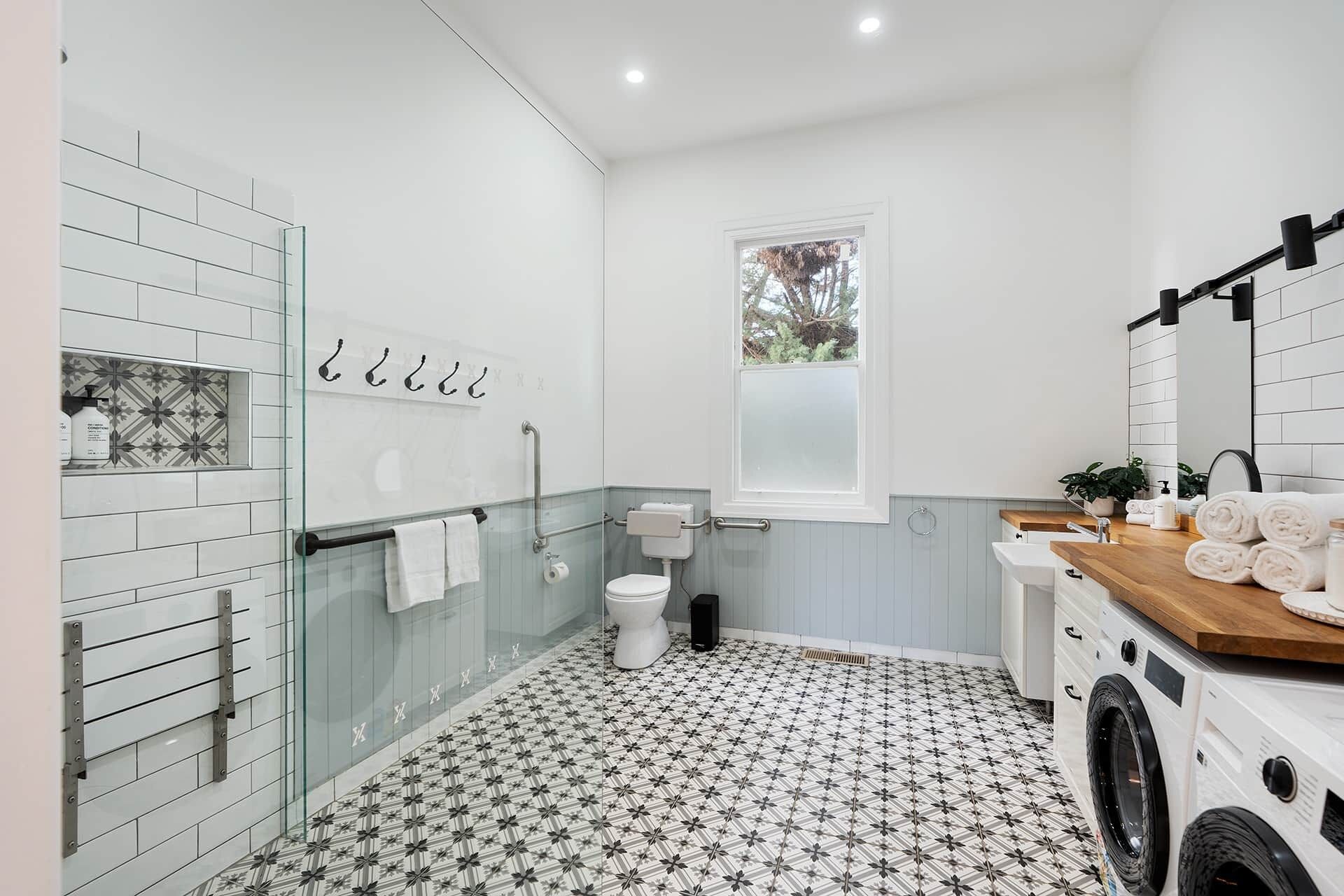 A modern bathroom with a glass shower enclosure, a toilet, a sink with a wooden countertop, and a washing machine.