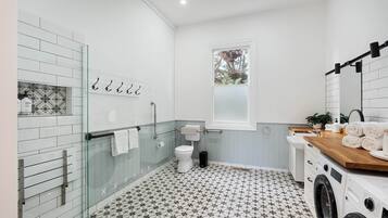 A modern bathroom with a glass shower enclosure, a toilet, a sink with a wooden countertop, and a washing machine.