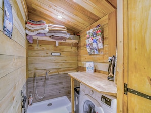 Ein Interieur einer Holzhütte mit Waschmaschine, Wäscheständer und einem Stapel Handtücher.