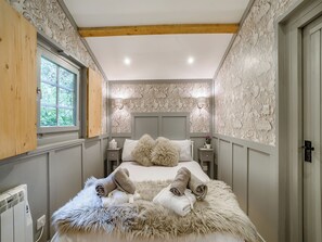 A bedroom with a large bed, a window, a nightstand, and a wall with intricate patterns.