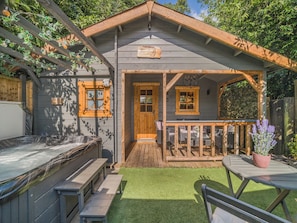 Eine Holzhütte mit Veranda, überdachter Sitzgelegenheit und kleinem Garten.