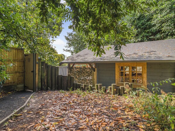 A wooden house with a covered porch, a wooden fence, and a leaf-covered ground.