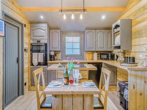 A kitchen with wooden cabinets, a dining table with chairs, a refrigerator, a microwave, and a window.