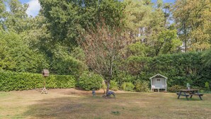Un espacio al aire libre con césped, una casita de pájaros de madera, una mesa de picnic y un cobertizo pequeño.
