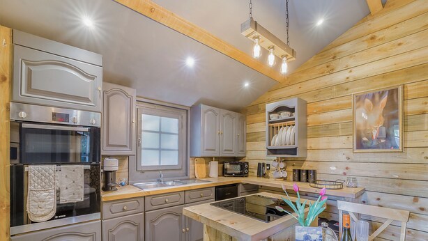 Una cocina con armarios de madera, un horno Bosch, un lavamanos y un comedor con una mesa lista para dos.