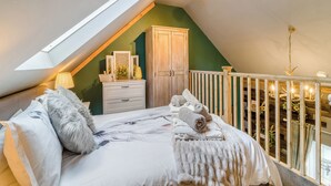 Un dormitorio con techo inclinado, un armario de madera, una cama con edredón blanco y una barandilla de balcón.