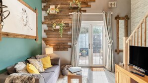 Una sala de estar con un sofá gris, vigas de madera, un televisor y vistas a través de puertas de cristal.