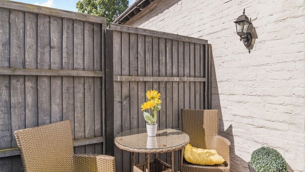 A patio with wicker chairs, a glass table, and a vase with sunflowers. - Coachmans Cottage - UK50418 (Ringwood, New Forest)
