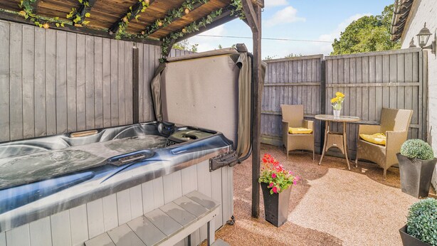 Un jacuzzi bajo una pérgola de madera, con valla de madera y mobiliario exterior.