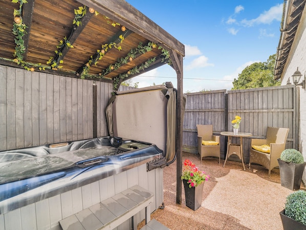 Un jacuzzi bajo una pérgola de madera, con valla de madera y mobiliario exterior.