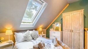 Un dormitorio con tragaluces, una cama con ropa de cama blanca, una mesita de noche con lámpara y un armario de madera.