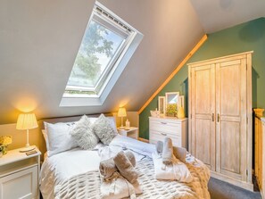 Un dormitorio con tragaluces, una cama con ropa de cama blanca, una mesita de noche con lámpara y un armario de madera.