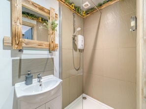 Un baño con un lavamanos blanco, un espejo con marco de madera, una ducha con cabezal de ducha manual y paredes con azulejos color beige.