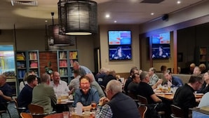 Un restaurant avec des tables et des chaises rondes, un écran de télévision et un tapis à motifs.