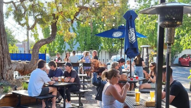 Un espace extérieur aménagé pour les repas, avec des tables et des chaises, entouré d’arbres et agrémenté d’un parasol bleu.