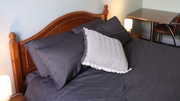 A neatly made bed with a wooden headboard, a small bedside table with a lamp, and a framed picture on the wall.