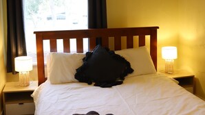 Un lit bien fait, avec des draps blancs, une tête de lit en bois et deux lampes de chevet.