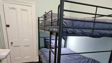 A dormitory room with bunk beds, a white door, a sink, and a small desk.