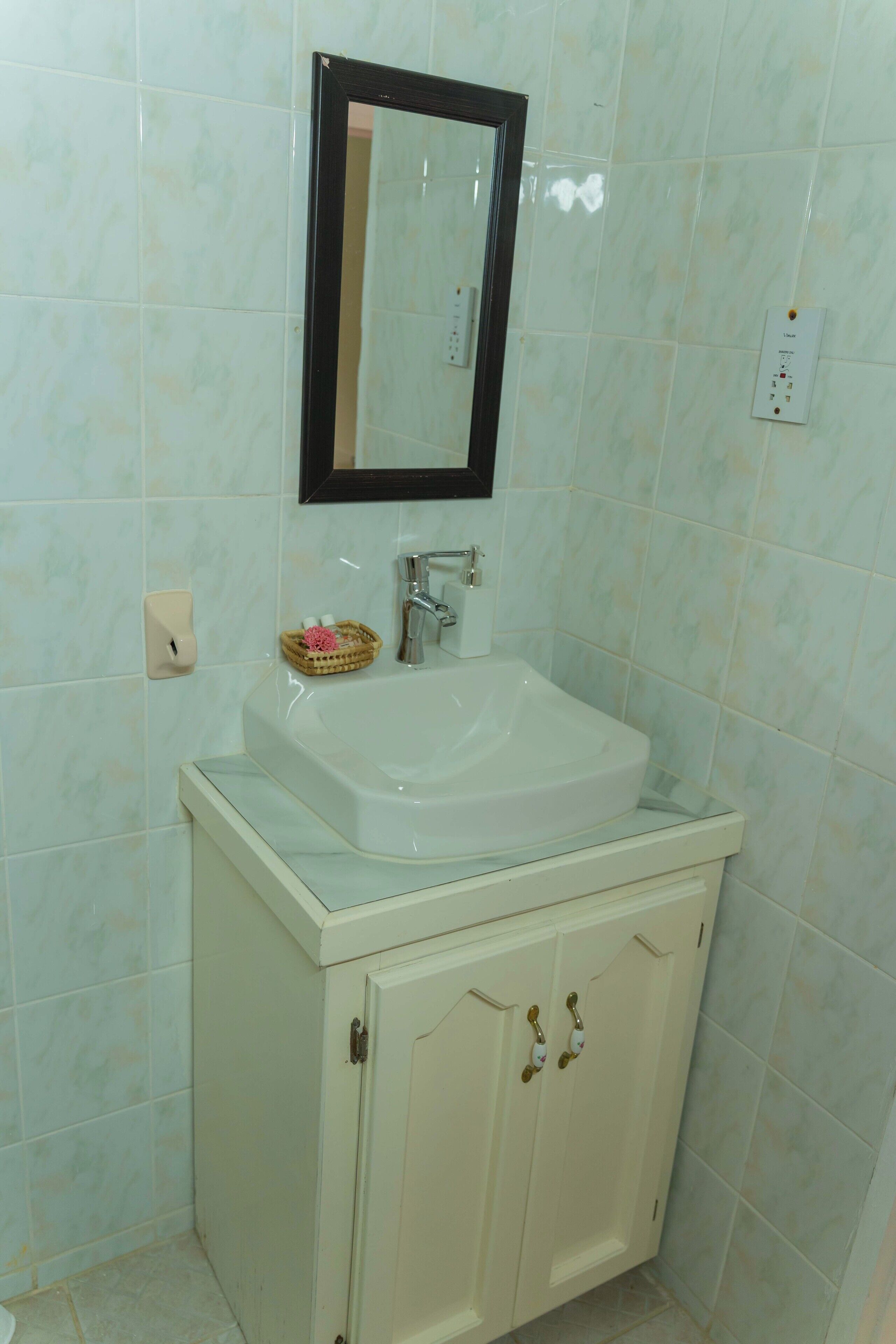 Een badkamer met een wit wastafelmeubel, een spiegel erboven en een kast eronder.