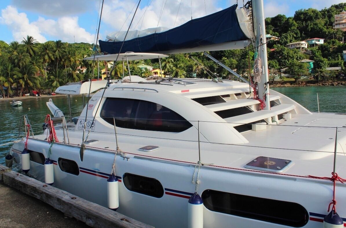 A white yacht docked at a marina with a covered deck, surrounded by palm trees and houses.