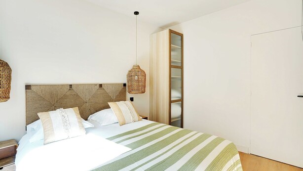 Un lit bien fait, avec une couvre-lit à rayures, une tête de lit en bois et deux lampes en osier.