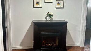 Ein Zimmer mit Kamin, Holzboden und drei gerahmten Kunstwerken an der Wand.