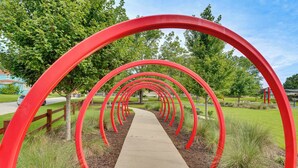 Ein Weg, der von roten Bögen gesäumt ist, führt durch einen Park mit Bäumen und Gras.