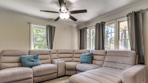 Ein beiges Ecksofa mit zwei blauen Kissen, einem Deckenventilator und einem Fenster mit Vorhängen.