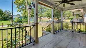 Eine überdachte Veranda mit Deckenventilator, weißer Reling und Blick auf eine Wohngegend mit Bäumen und Rasen.