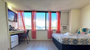 A hotel room with a bed, desk, chair, and a view of the mountains. - Family/Friends Hotel in Terrific Honolulu  Room, AC (Honolulu)