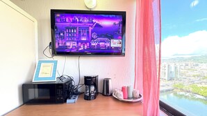 A hotel room with a TV displaying a cityscape, a coffee maker, a microwave, and a view of the city through the window. - Family/Friends Hotel in Terrific Honolulu  Room, AC (Honolulu)