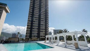 A rooftop pool with a white pergola, a tall building in the background, and palm trees. - Family/Friends Hotel in Terrific Honolulu  Room, AC (Honolulu)
