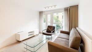 Een moderne woonkamer met een glazen salontafel, een bruine leren fauteuil, een beige bank en een witte tv-meubel.