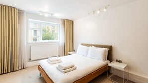 Een moderne hotelkamer met een houten bed, witte lakens, een nachtkastje en een raam met gordijnen.