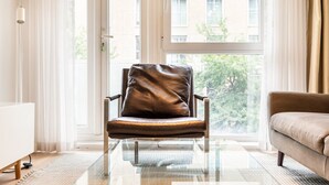 Een moderne woonkamer met een leren fauteuil, een glazen salontafel en een beige bank.