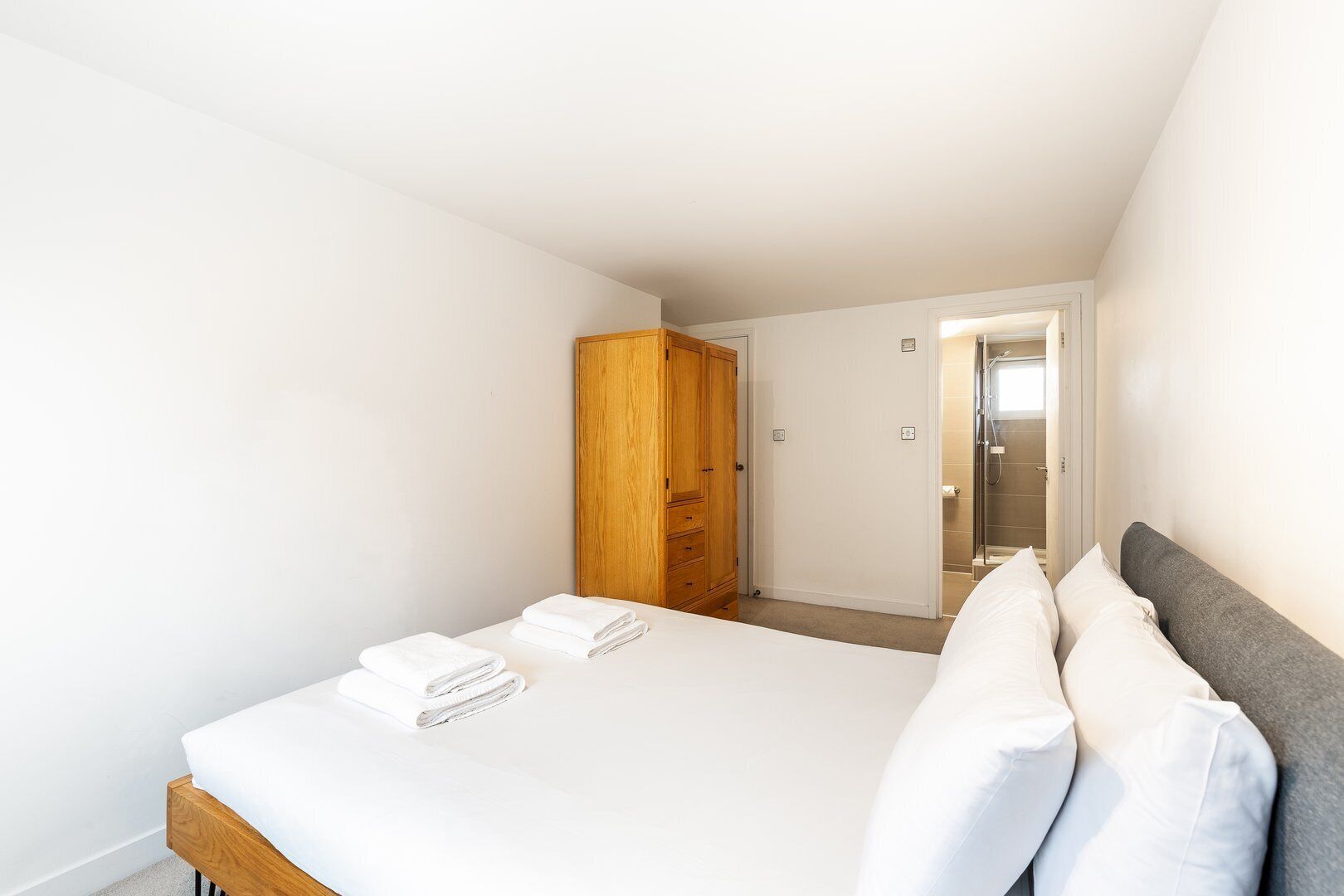 Ein Schlafzimmer mit einem Bett, einem Holzschrank und einem sichtbaren Duschbereich durch eine offene Tür.