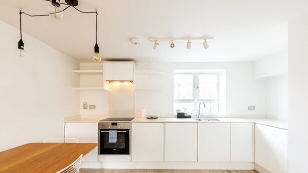 Een moderne keuken met witte kasten, een houten eettafel en een inbouwoven.