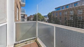 Ein Balkon mit Metallgeländer, Blick auf angrenzende Gebäude und einem strahlend blauen Himmel.
