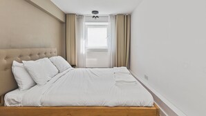Ein ordentlich bezogenes Bett mit weißen Leinen, einem gepolsterten Kopfteil und einem Holzrahmen.
