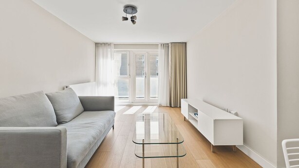 Ein modernes Wohnzimmer mit einem grauen Sofa, einem Glastisch und einer weißen TV-Konsole.
