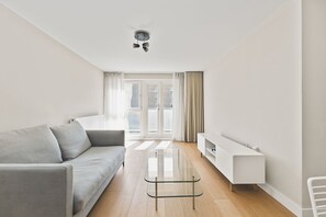 Ein modernes Wohnzimmer mit einem grauen Sofa, einem Glastisch und einer weißen TV-Konsole.