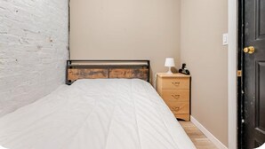 Une chambre à coucher comprenant un lit, une tête de lit en bois, une table de chevet avec une lampe et une commode.