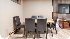 Un coin repas avec une table en bois et quatre chaises, un téléviseur fixé au mur et un petit meuble sur le côté droit.