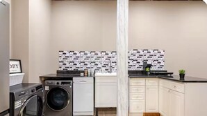 Une cuisine compacte équipée d’un lave-linge, d’un lave-vaisselle et d’un crédence carrelée.