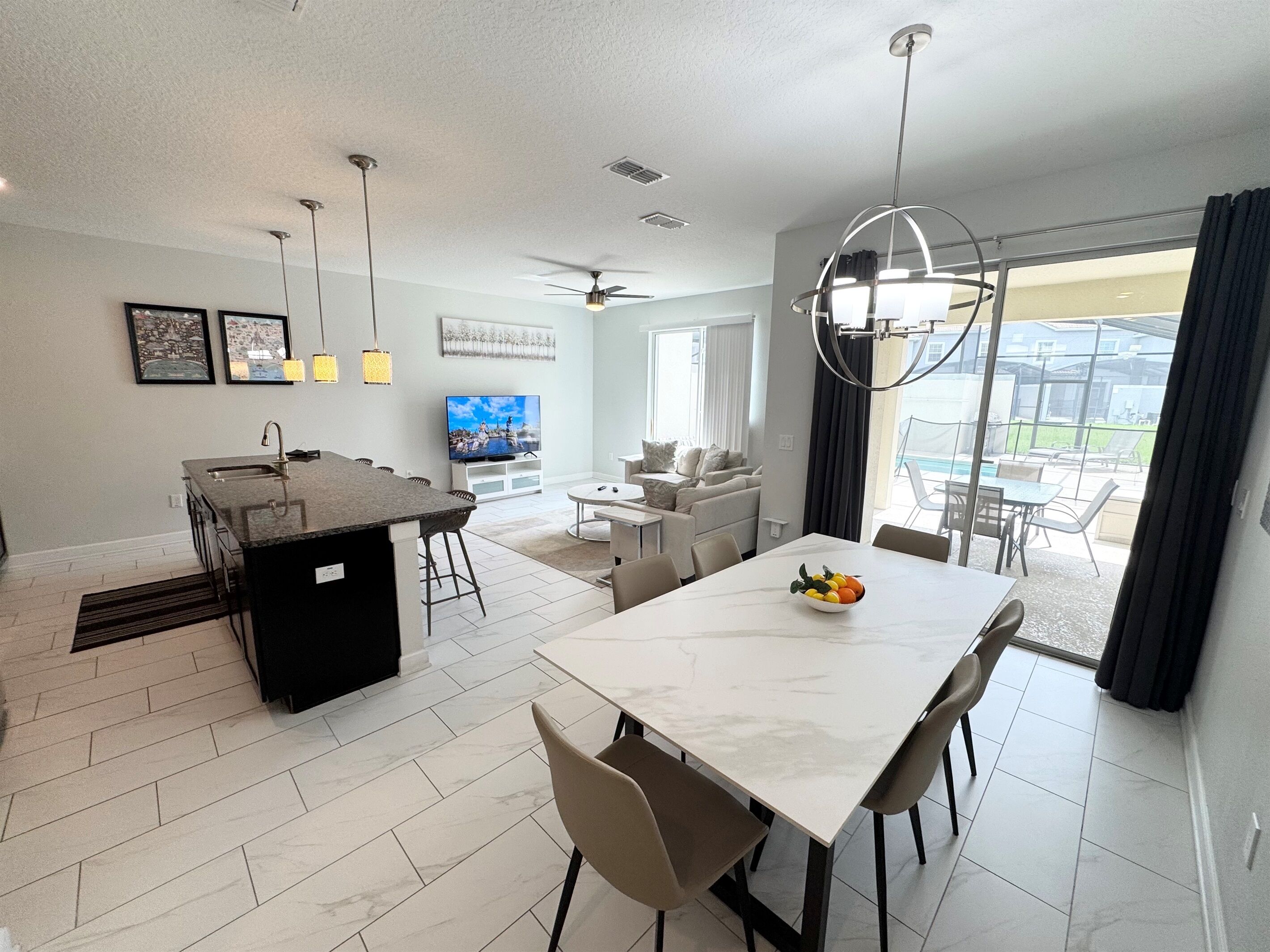 Una cocina moderna con una isla central, un comedor con una mesa blanca y una sala de estar con sofá y televisor.
